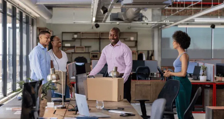 Team meeting in an office with four people gathered around a table and cardboard boxes.