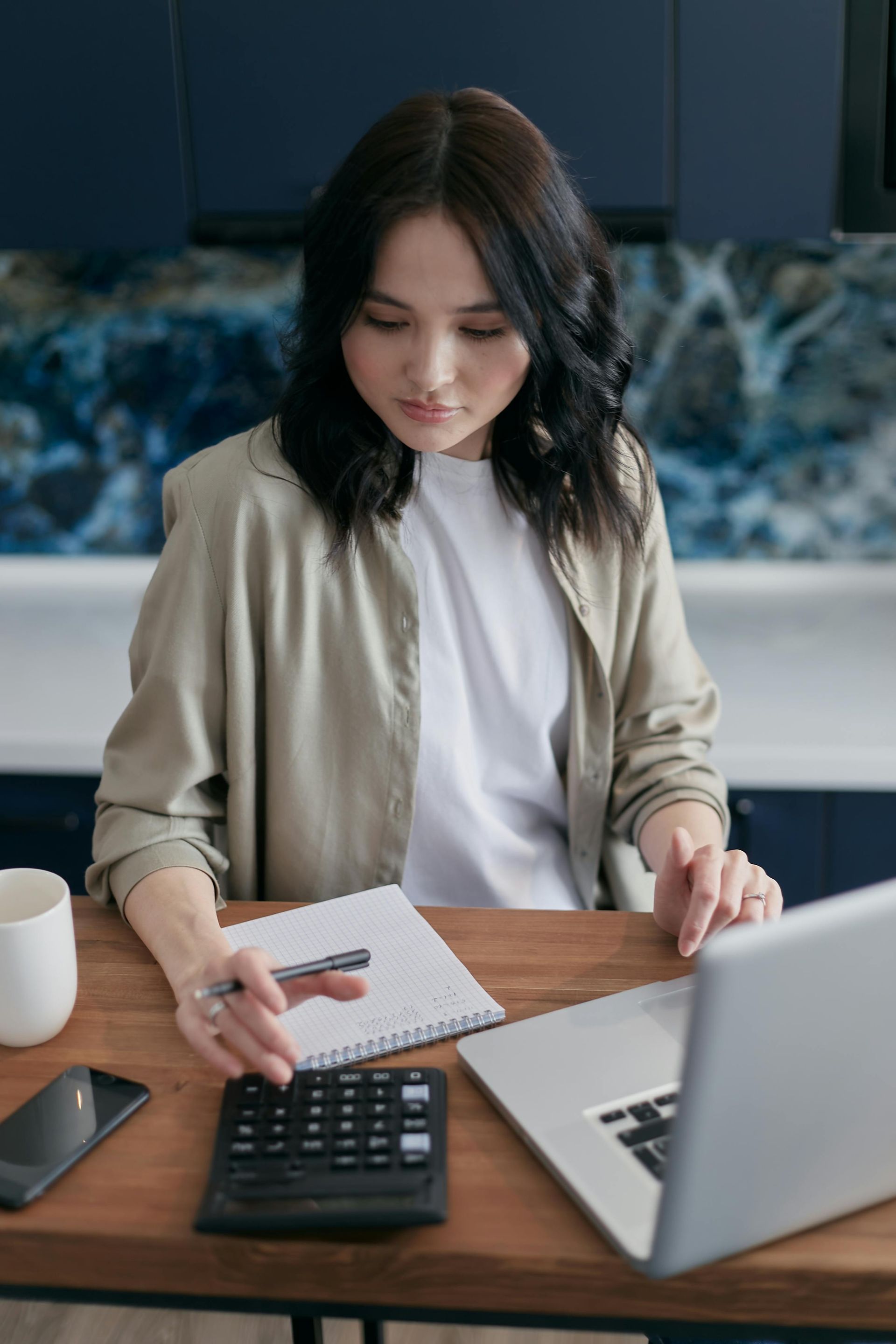 Woman at a desk reviewing papers beside a laptop and calculator in an office.