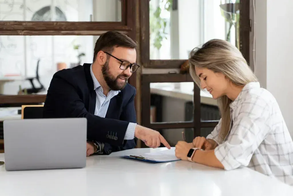 Two coworkers reviewing documents at a table with a laptop in a bright office