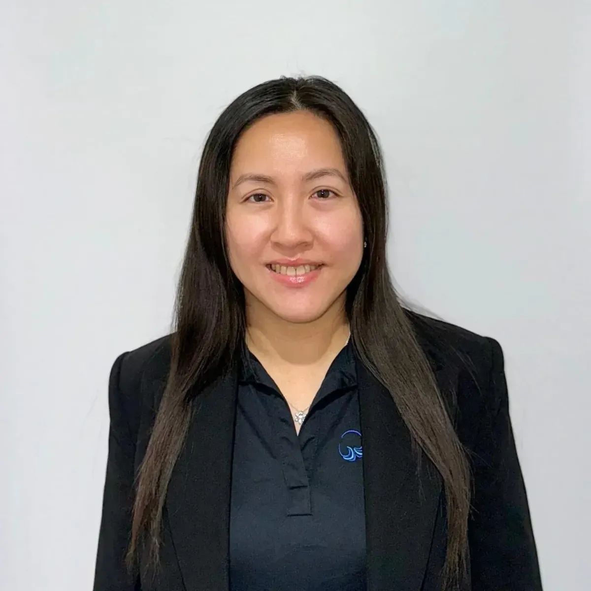 Portrait of a smiling woman in a black blazer against a light gray background