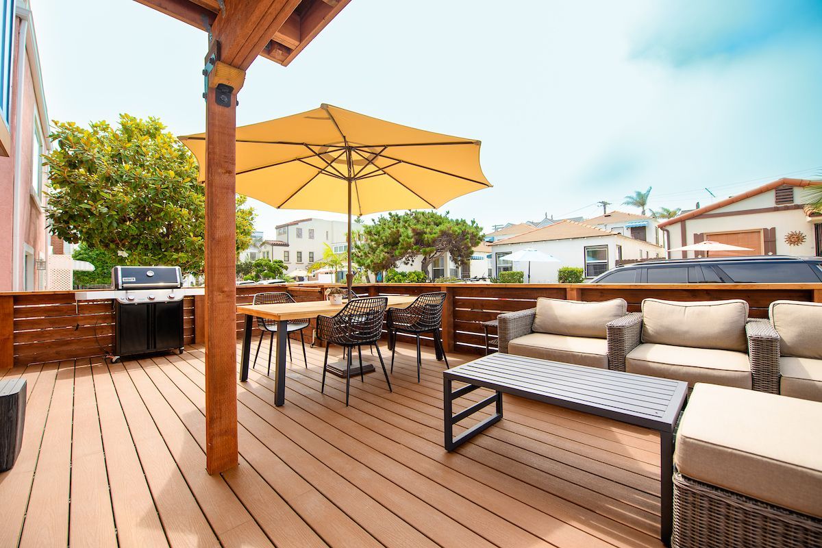 A wooden deck with a couch , table , chairs and an umbrella.