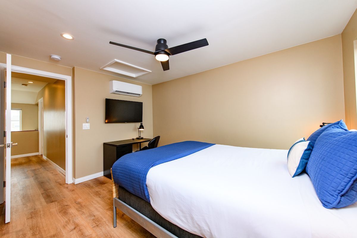 A hotel room with a bed , desk , television and ceiling fan.