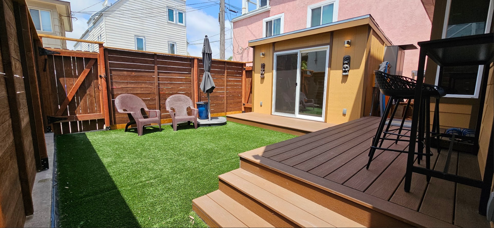A backyard with a deck , stairs , chairs and umbrellas.