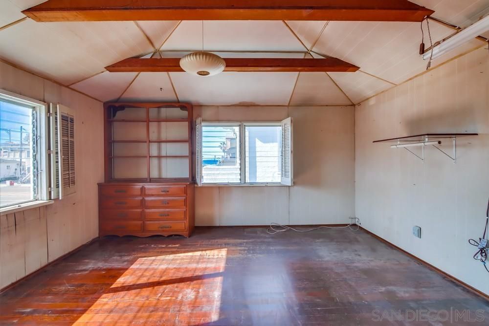 An empty room with a wooden floor , a dresser and a window.