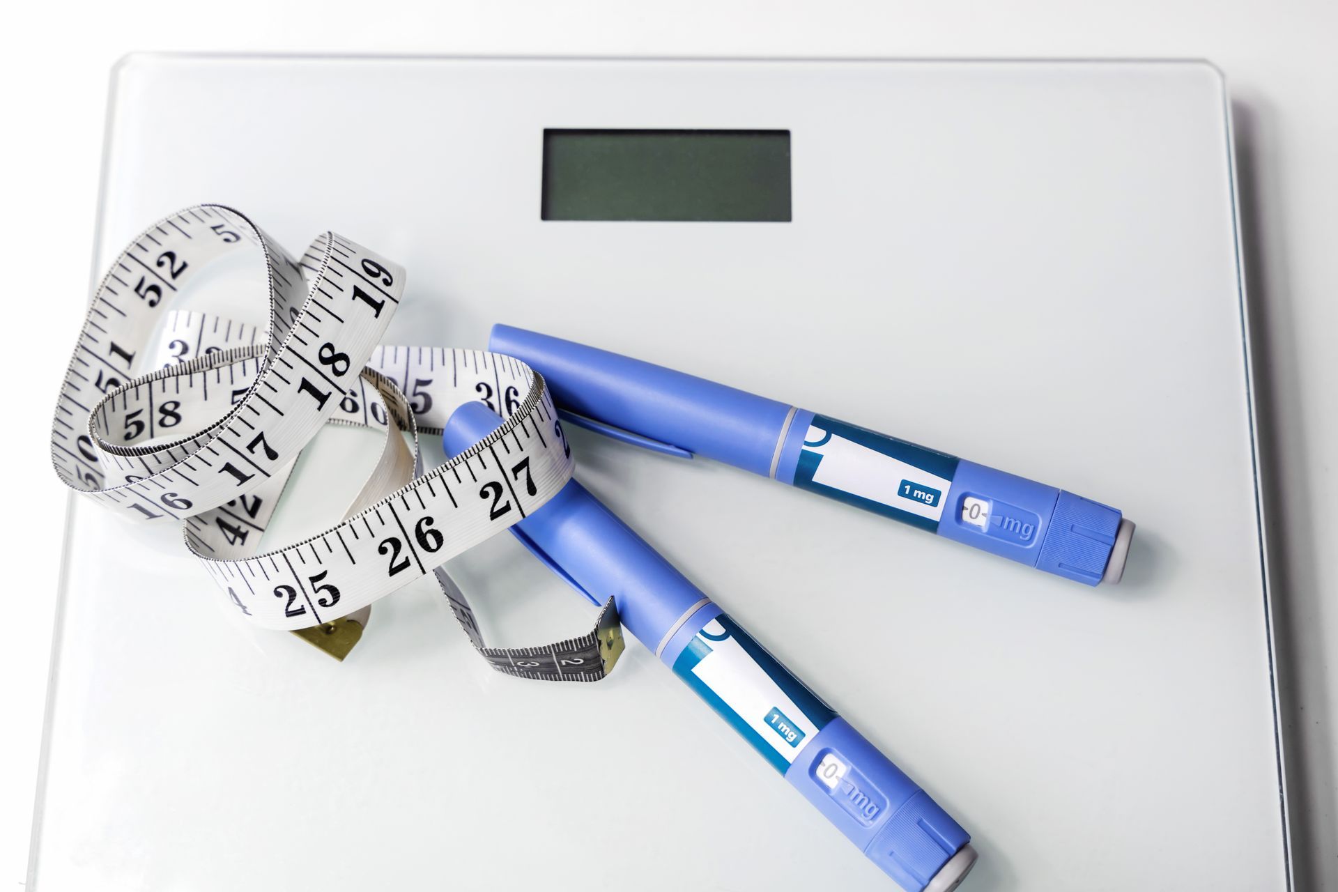 White bathroom scale with measuring tape and two blue insulin pens.