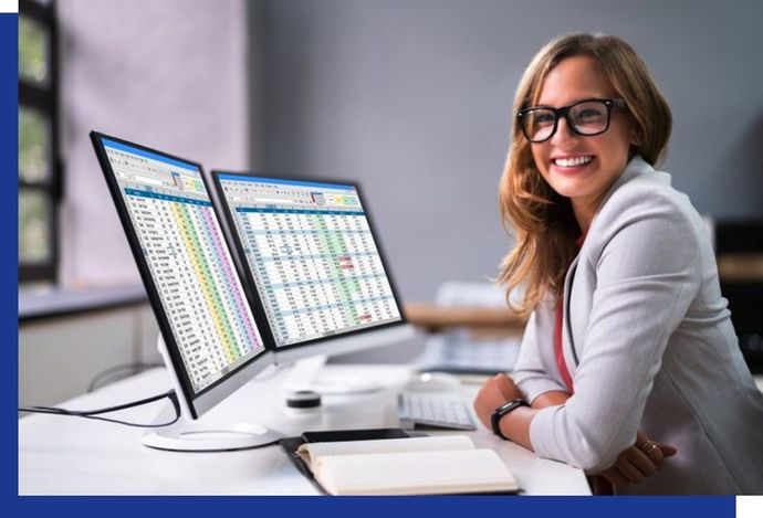 A woman is sitting at a desk in front of two computer monitors.