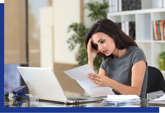 A woman is sitting at a desk with a laptop and a piece of paper.
