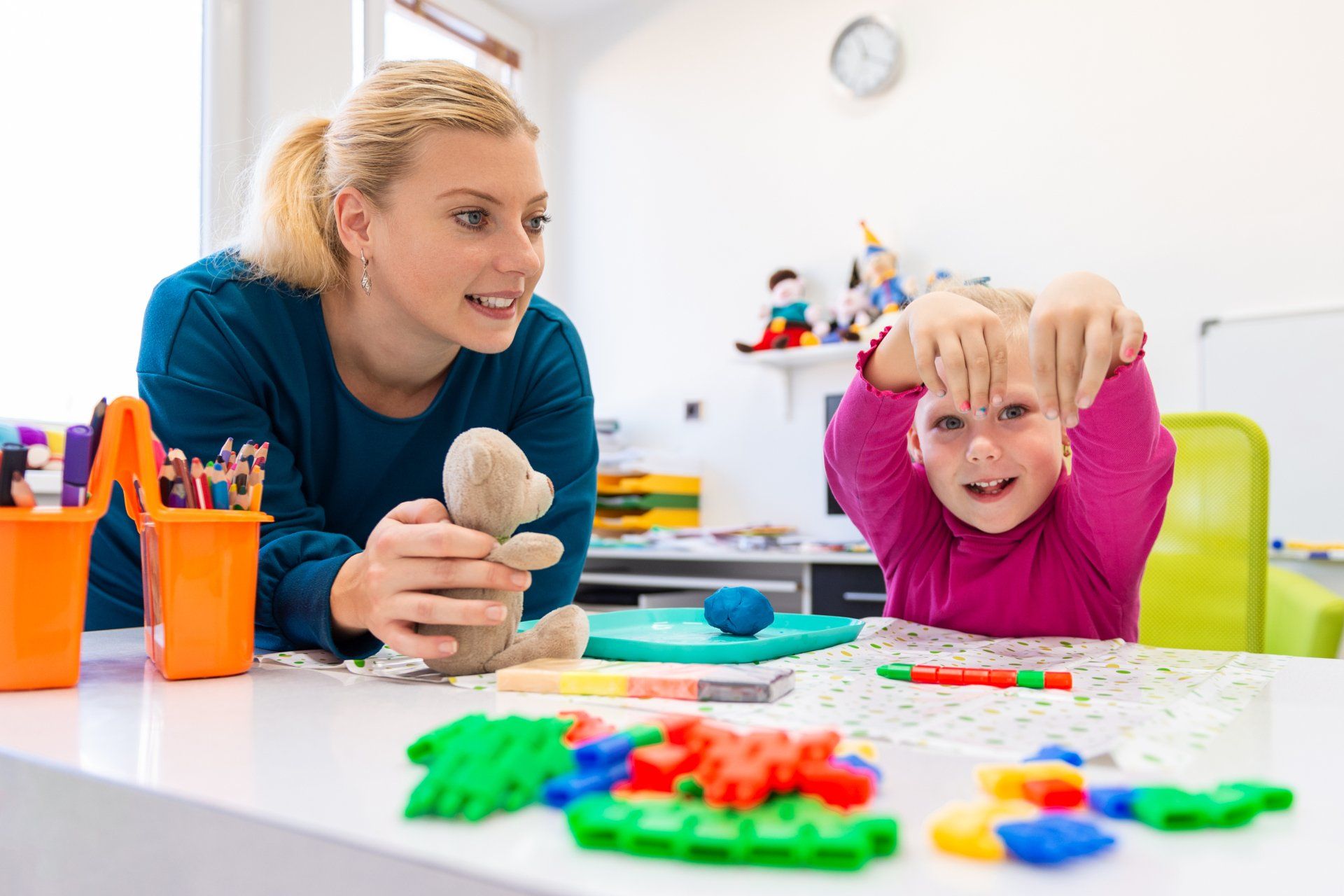 A woman is playing with a child at a table with toys.