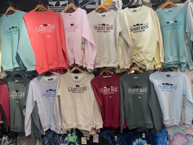 Stacked crewnecks with Western North Carolina and Lake Lure designs inside a mountain gift shop.