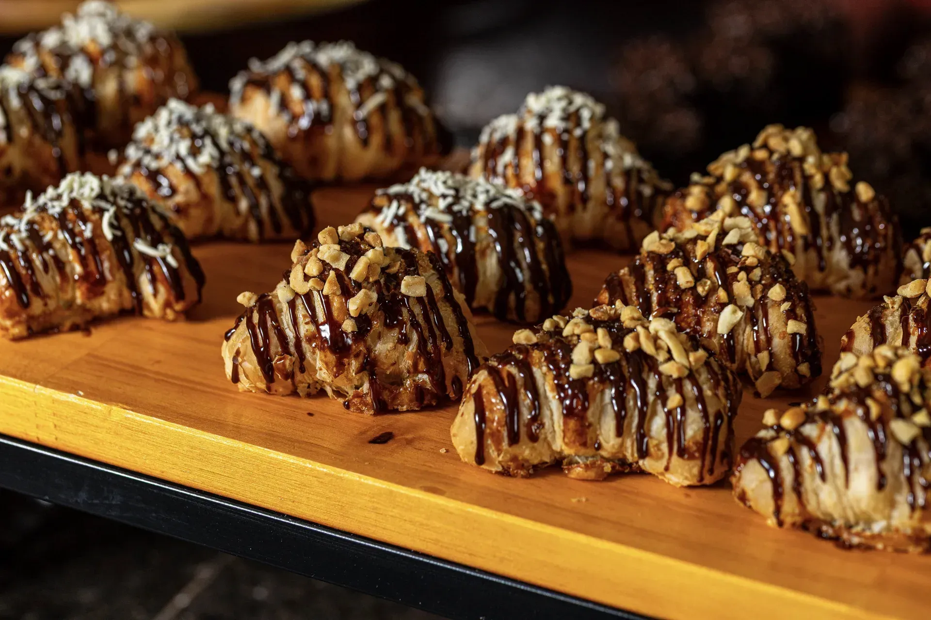 Uma tábua de corte de madeira coberta com croissants cobertos de chocolate e coco.