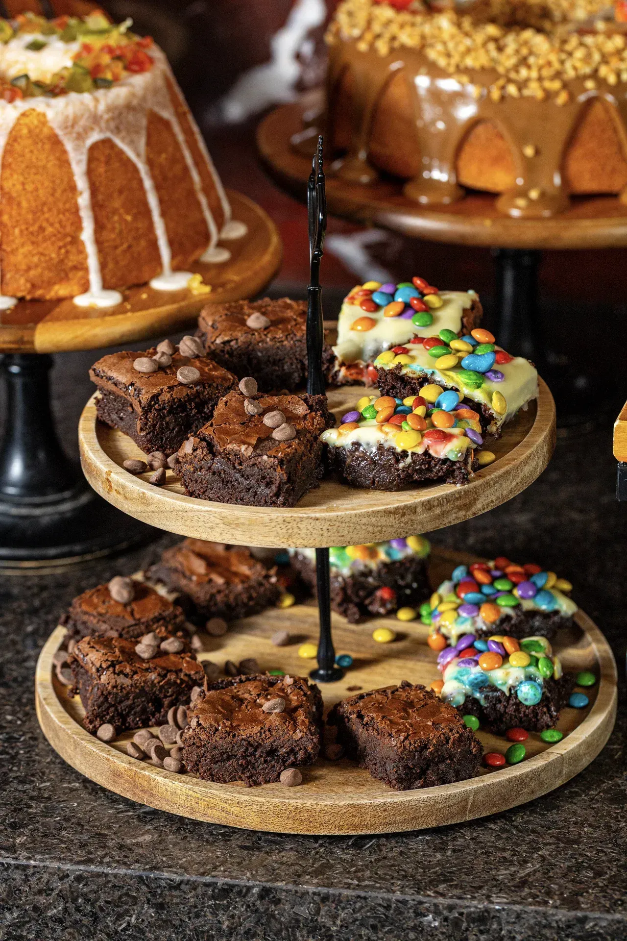 Uma bandeja de madeira cheia de brownies e cupcakes sobre uma mesa.