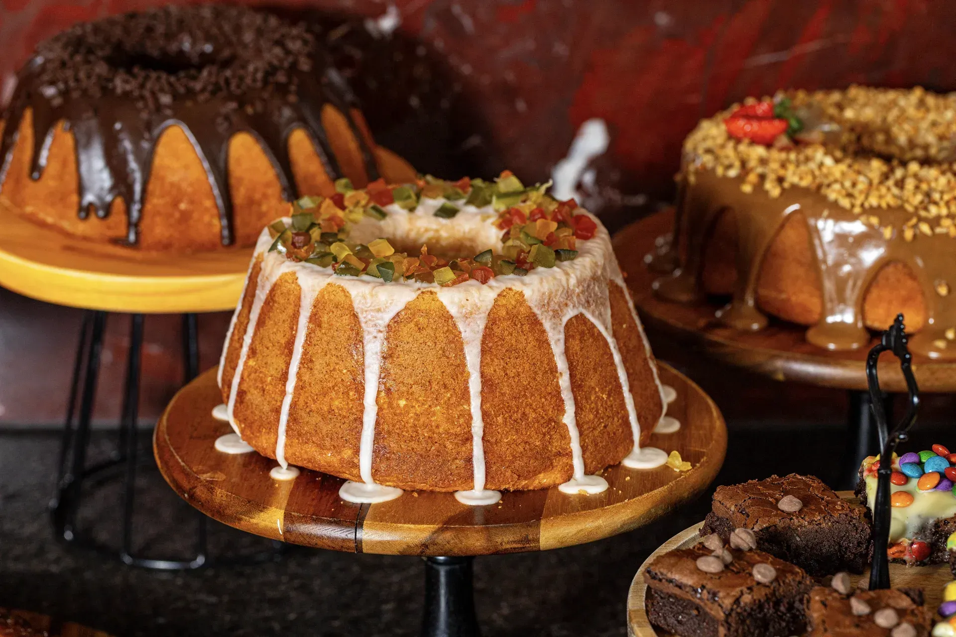 Três bolos bundt estão em uma bandeja de madeira sobre uma mesa.