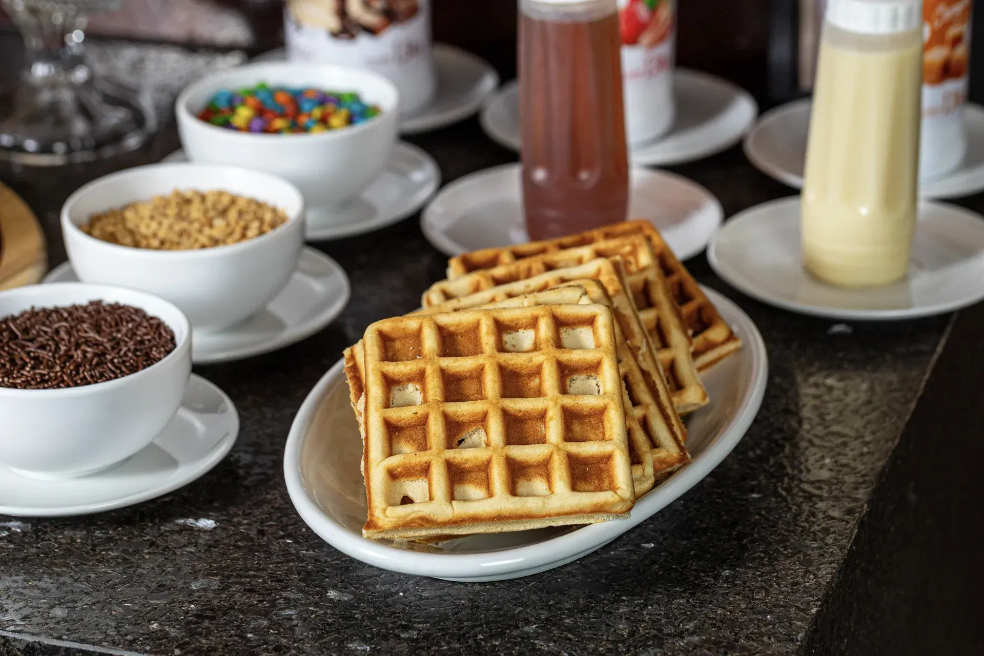 Um prato de waffles sobre uma mesa com tigelas de coberturas.