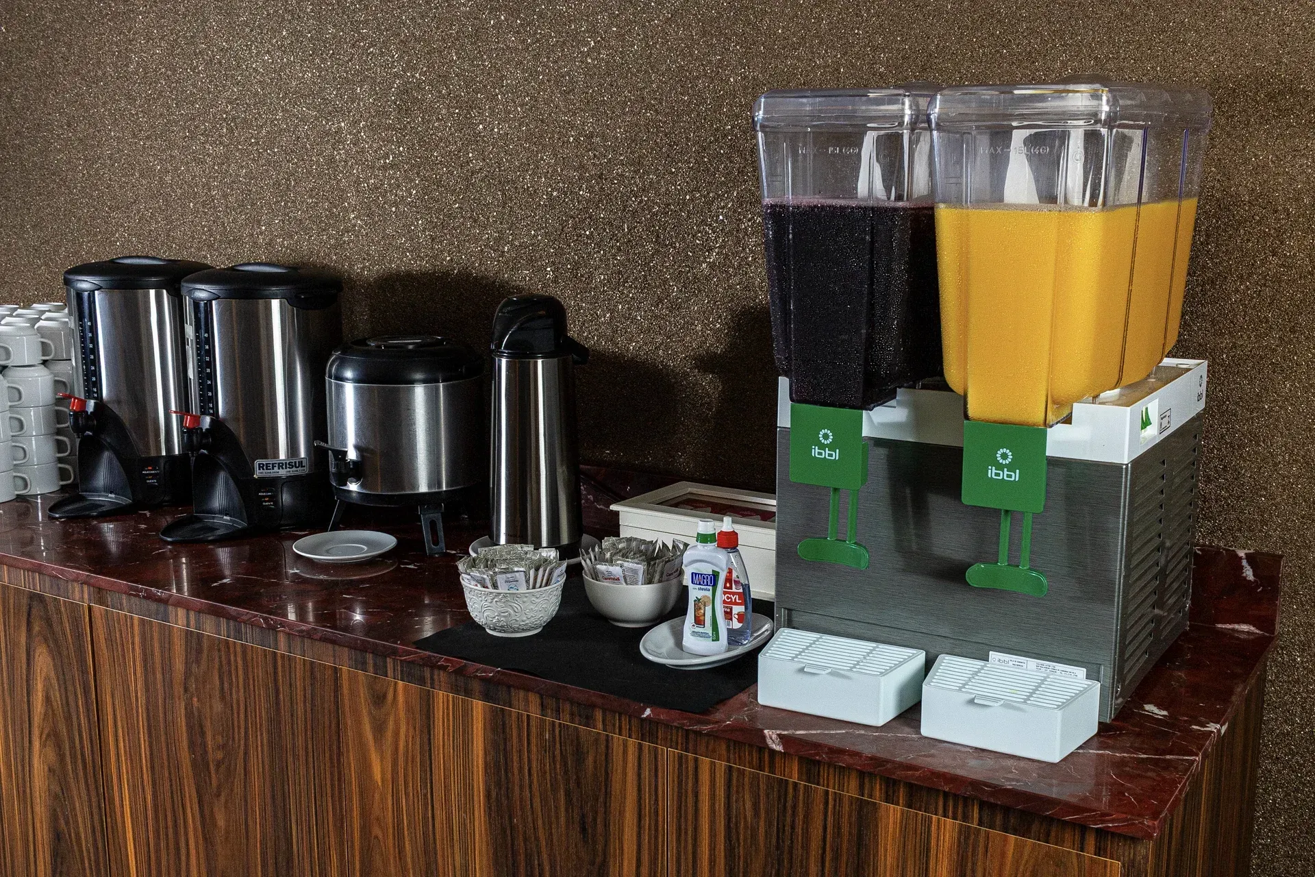 Uma mesa de bufê com um dispensador de bebidas cheio de suco de laranja.