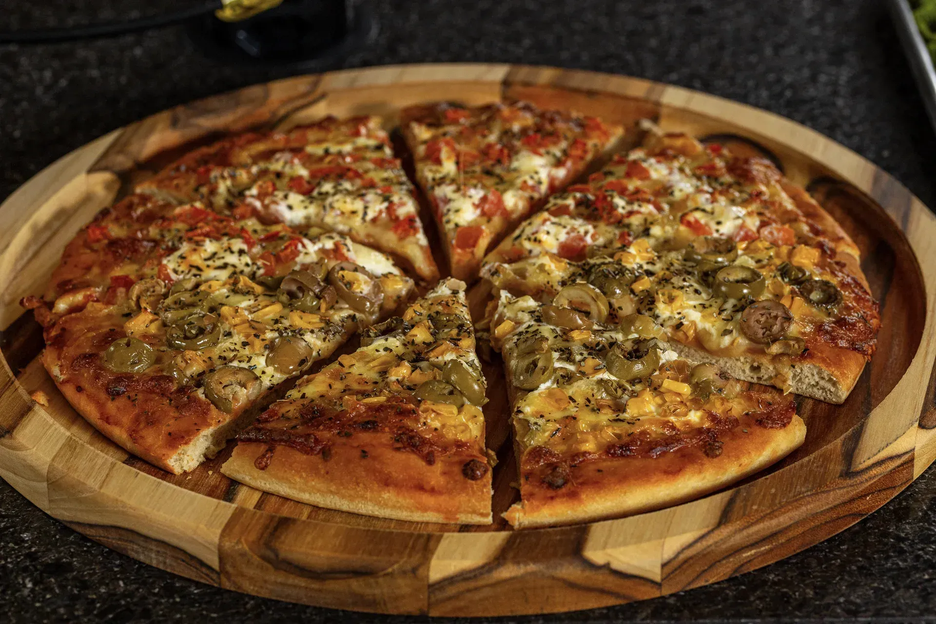 Uma pizza é cortada em fatias em uma tábua de corte de madeira.