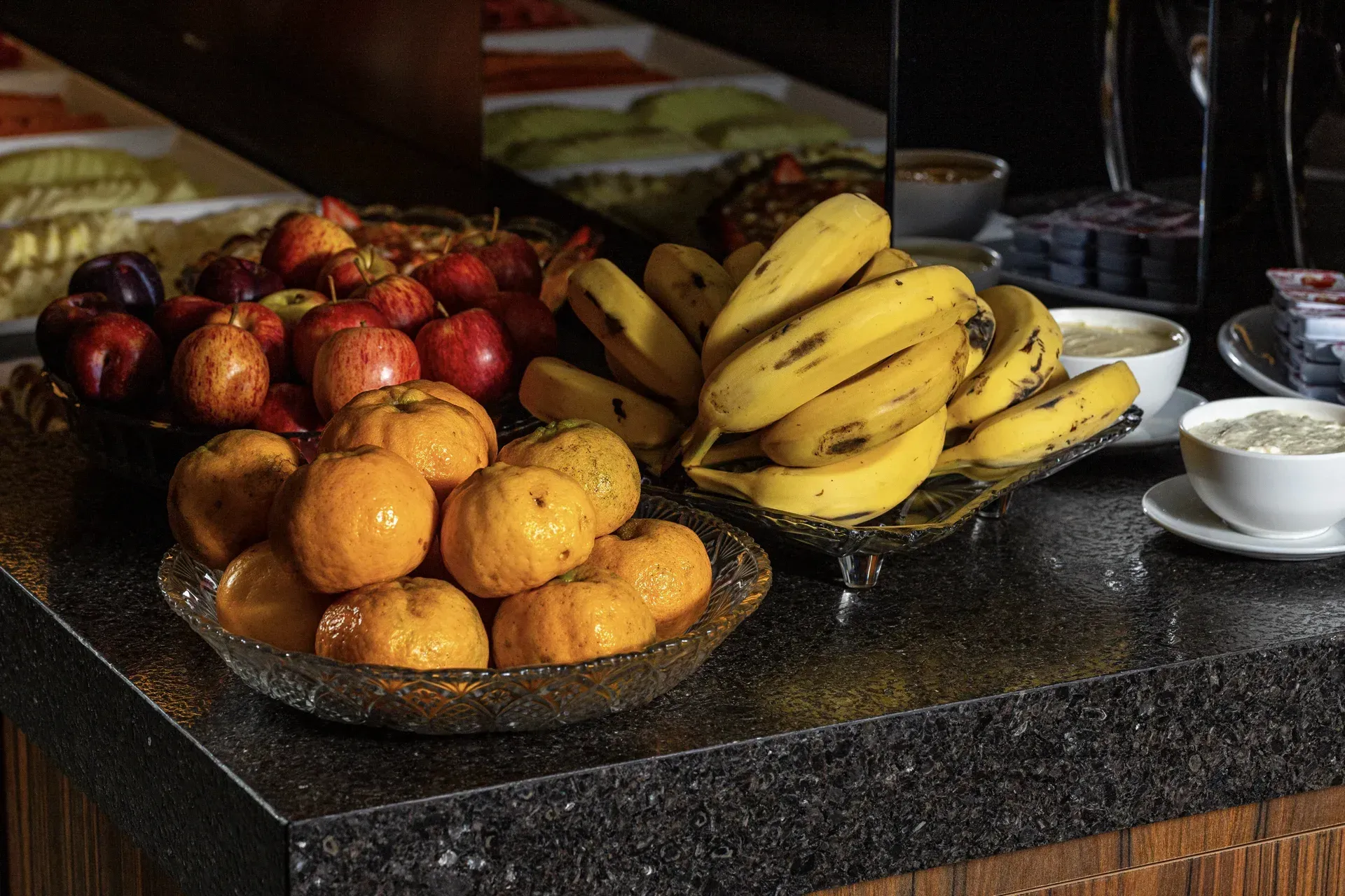 Uma tigela de bananas está em um balcão ao lado de uma tigela de frutas.