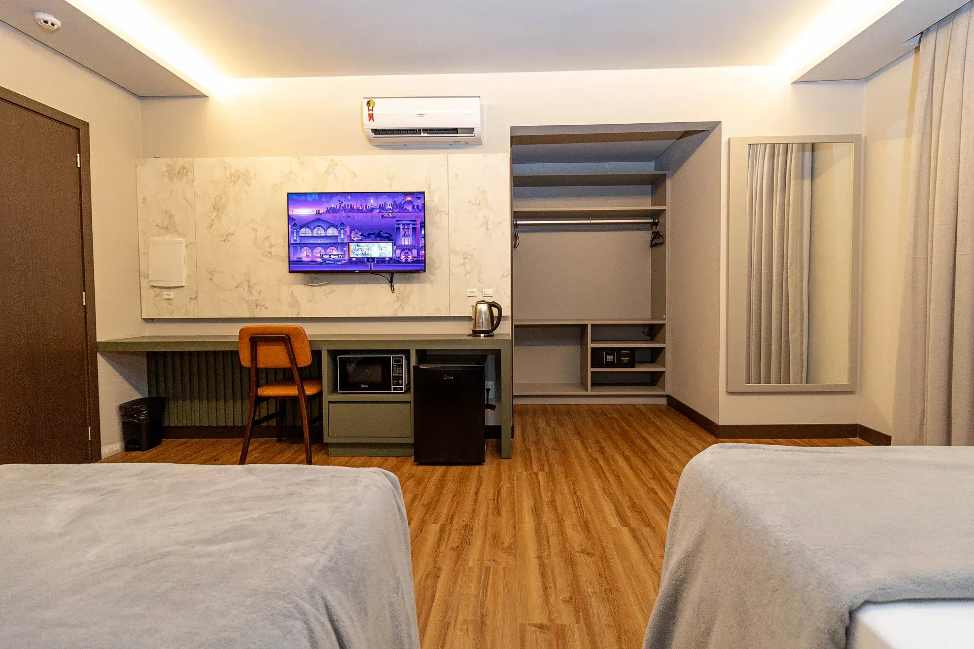 Um quarto de hotel com duas camas, uma escrivaninha e uma TV de tela plana.