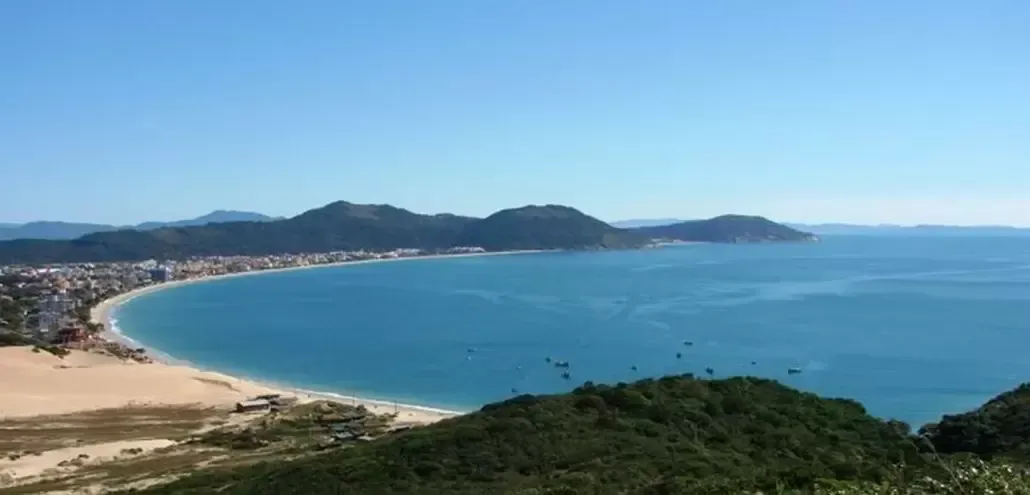 um grande corpo de água com montanhas ao fundo e uma praia em primeiro plano.