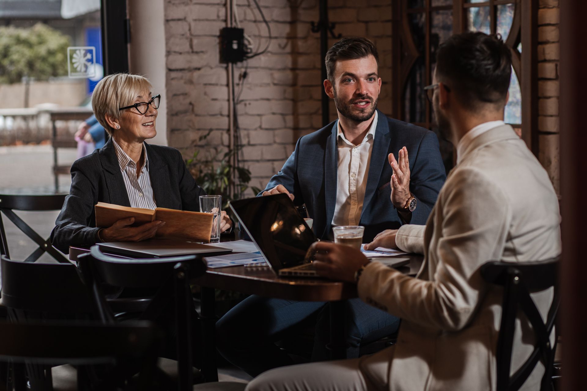 Three people in a meeting around a laptop at a café table, discussing work.