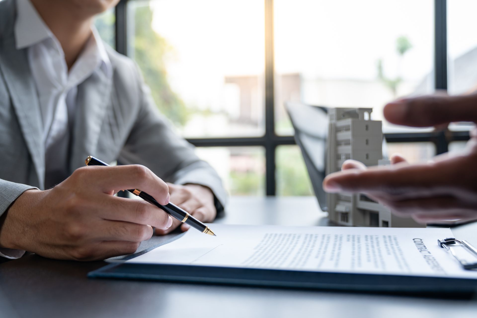 Two people reviewing documents and a model building at a desk in a bright office