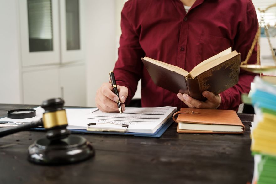 Person writing at a desk with an open book and a gavel nearby, suggesting legal work
