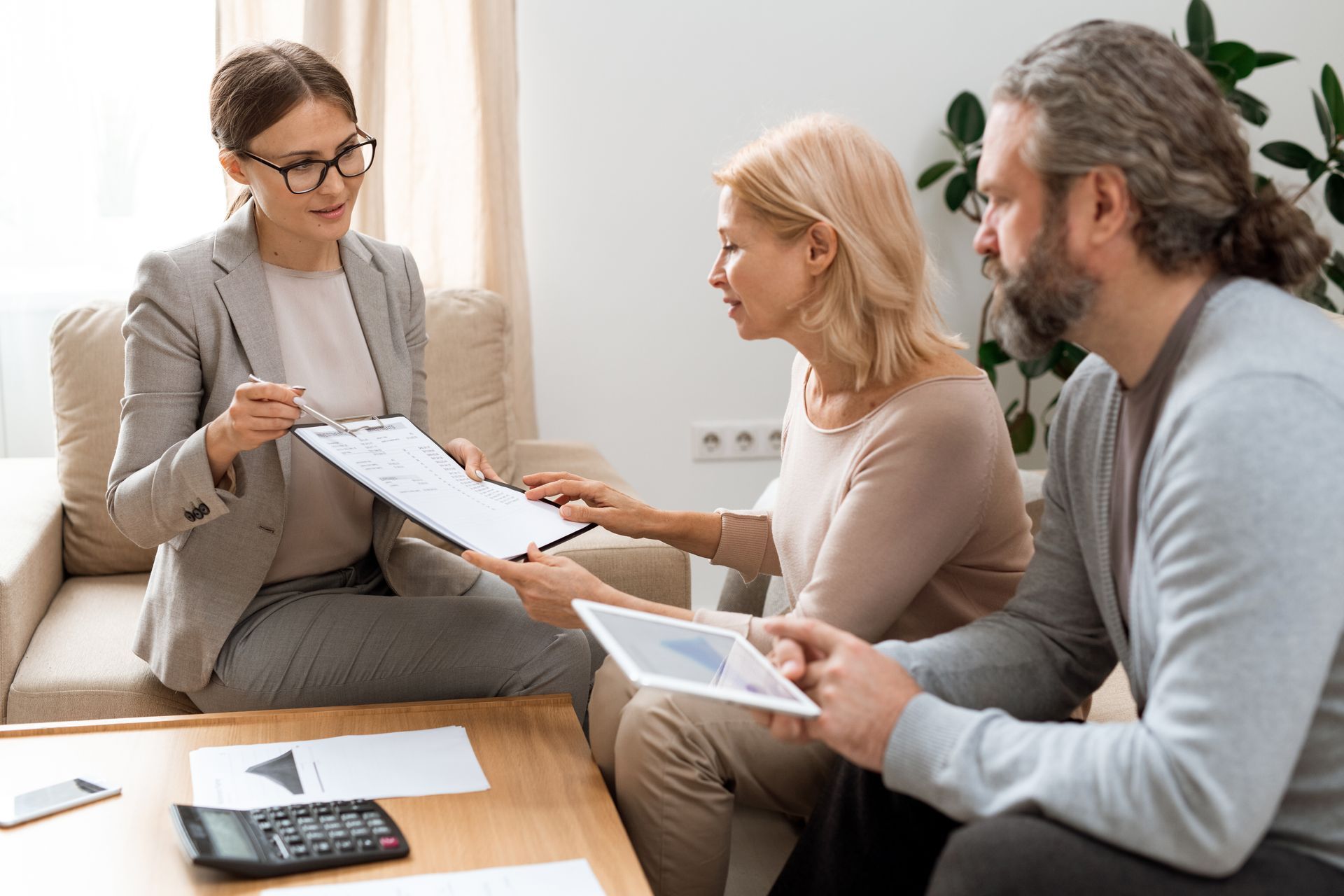 Three people discussing documents in a bright office, with a calculator and papers on the table.
