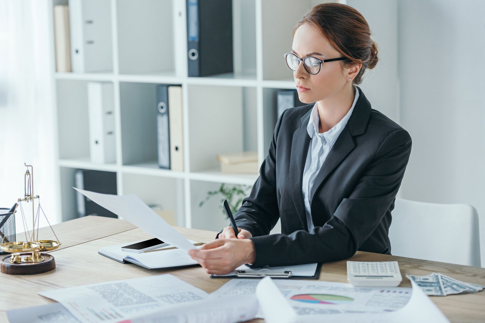 Office worker taking notes at a desk with papers, laptop, and binders in a bright office