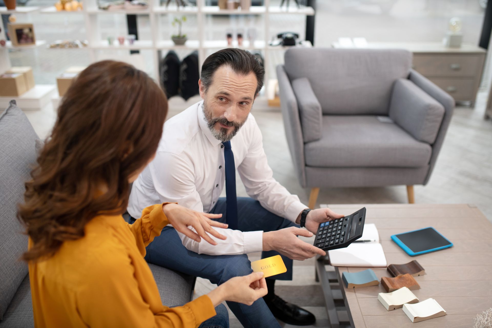 Two people discussing a yellow card in a bright office, with a laptop and paperwork on the table.