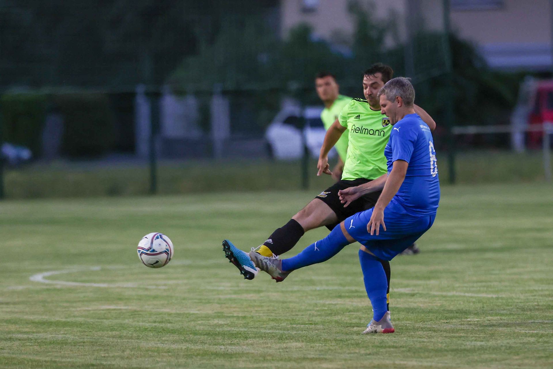 Deux hommes jouent au football sur un terrain et l'un d'eux frappe le ballon.