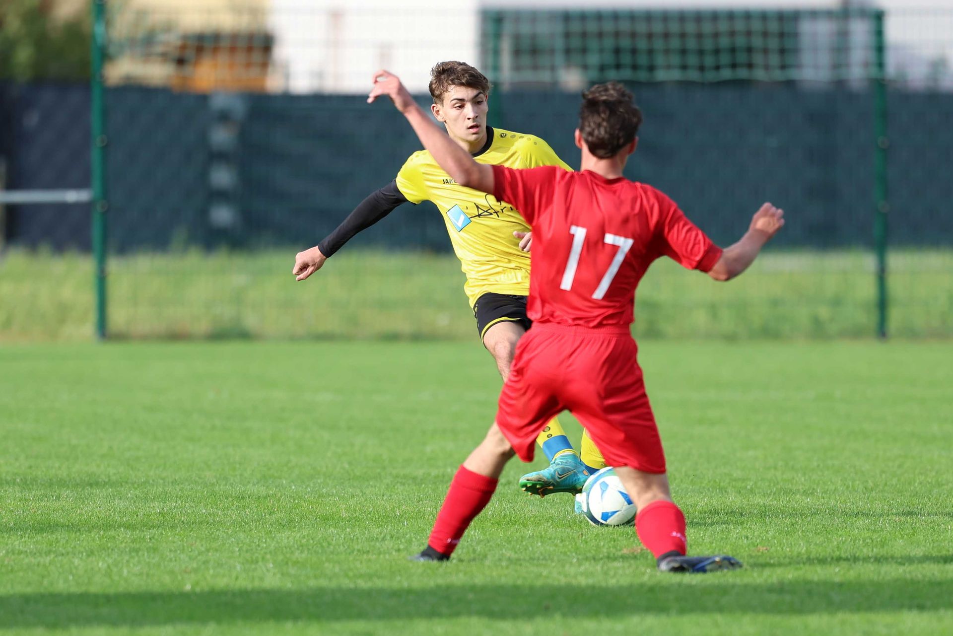 Deux garçons jouent au football sur un terrain et l'un d'eux porte un maillot rouge avec le numéro 17 dessus.