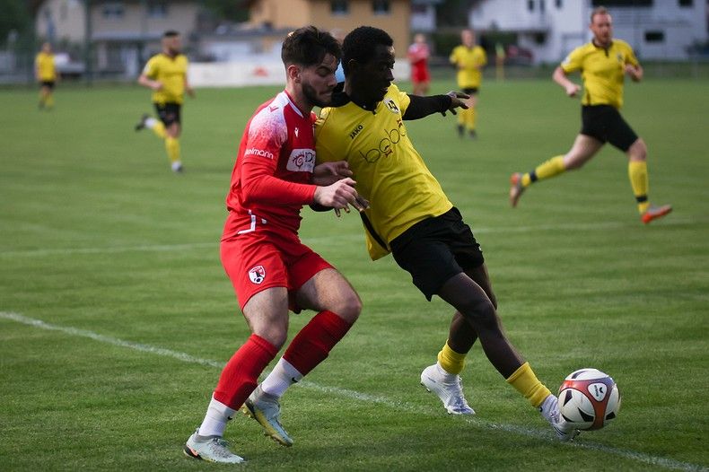 Deux joueurs de football se battent pour le ballon sur un terrain.