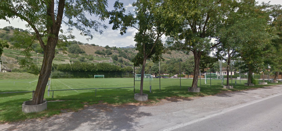 Un terrain de football entouré d'arbres à côté d'une route.