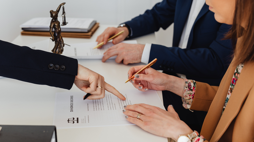 People in business attire reviewing documents and pointing at papers during a meeting.