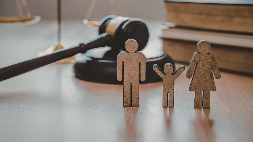 Miniature family figures beside a judge’s gavel on a desk, suggesting family law or custody.