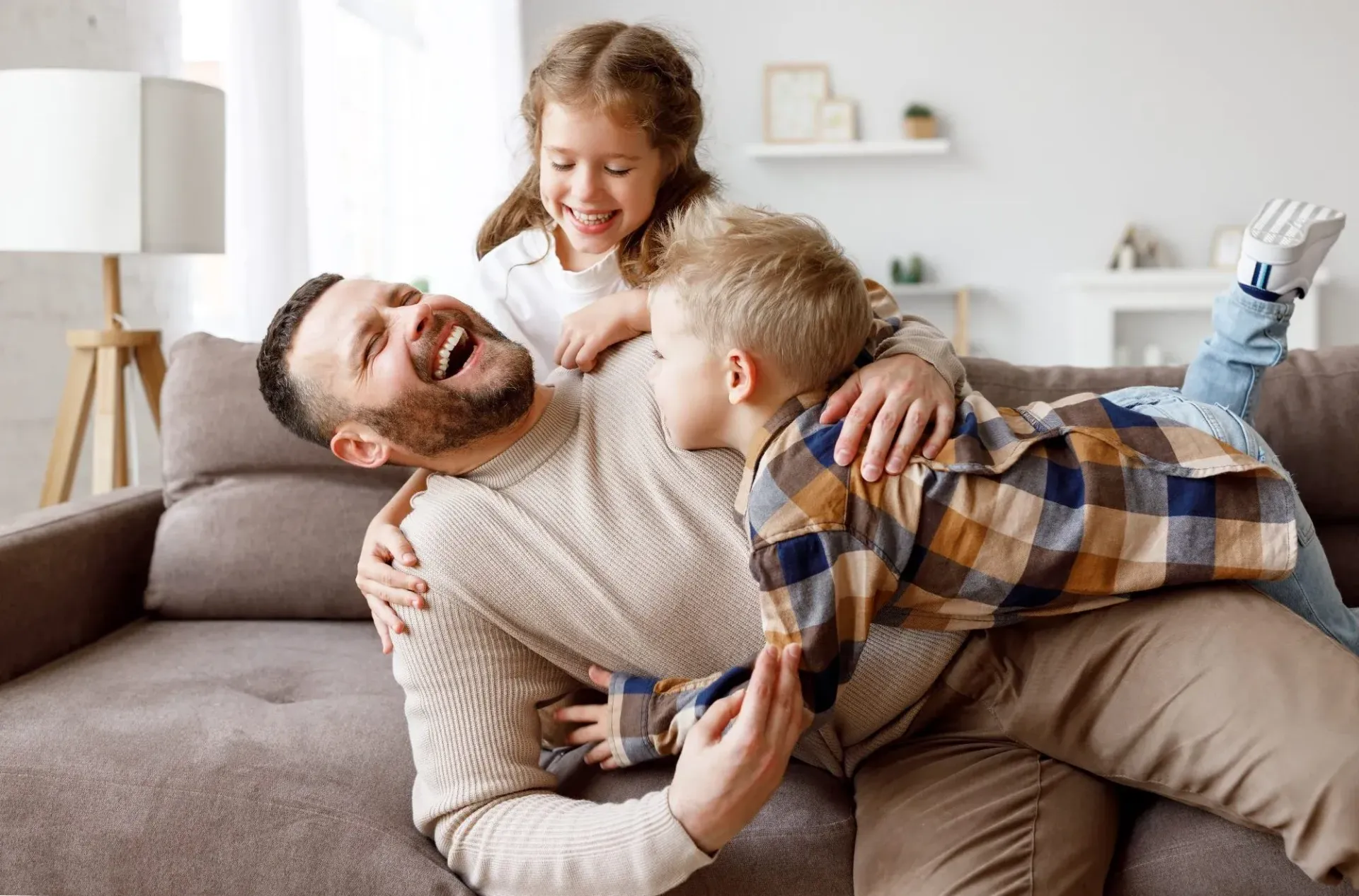 Child hugging teddy bear on couch while two adults argue in the background