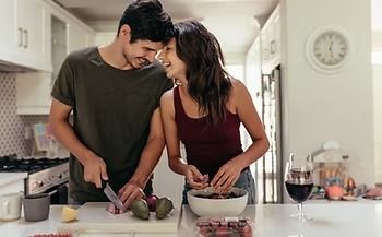Couple cooking together in a bright kitchen, smiling while chopping vegetables and mixing ingredients.