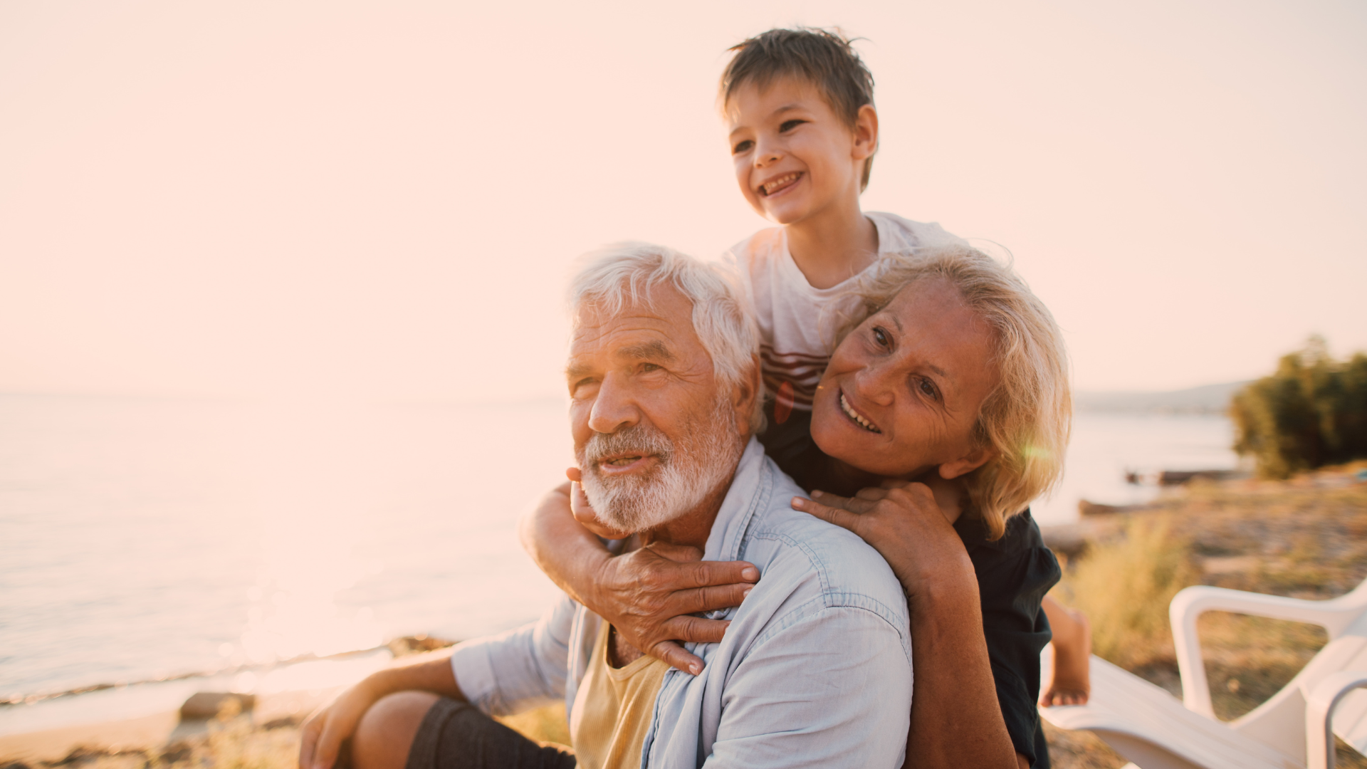 Three generations smiling together outdoors at sunset by the water