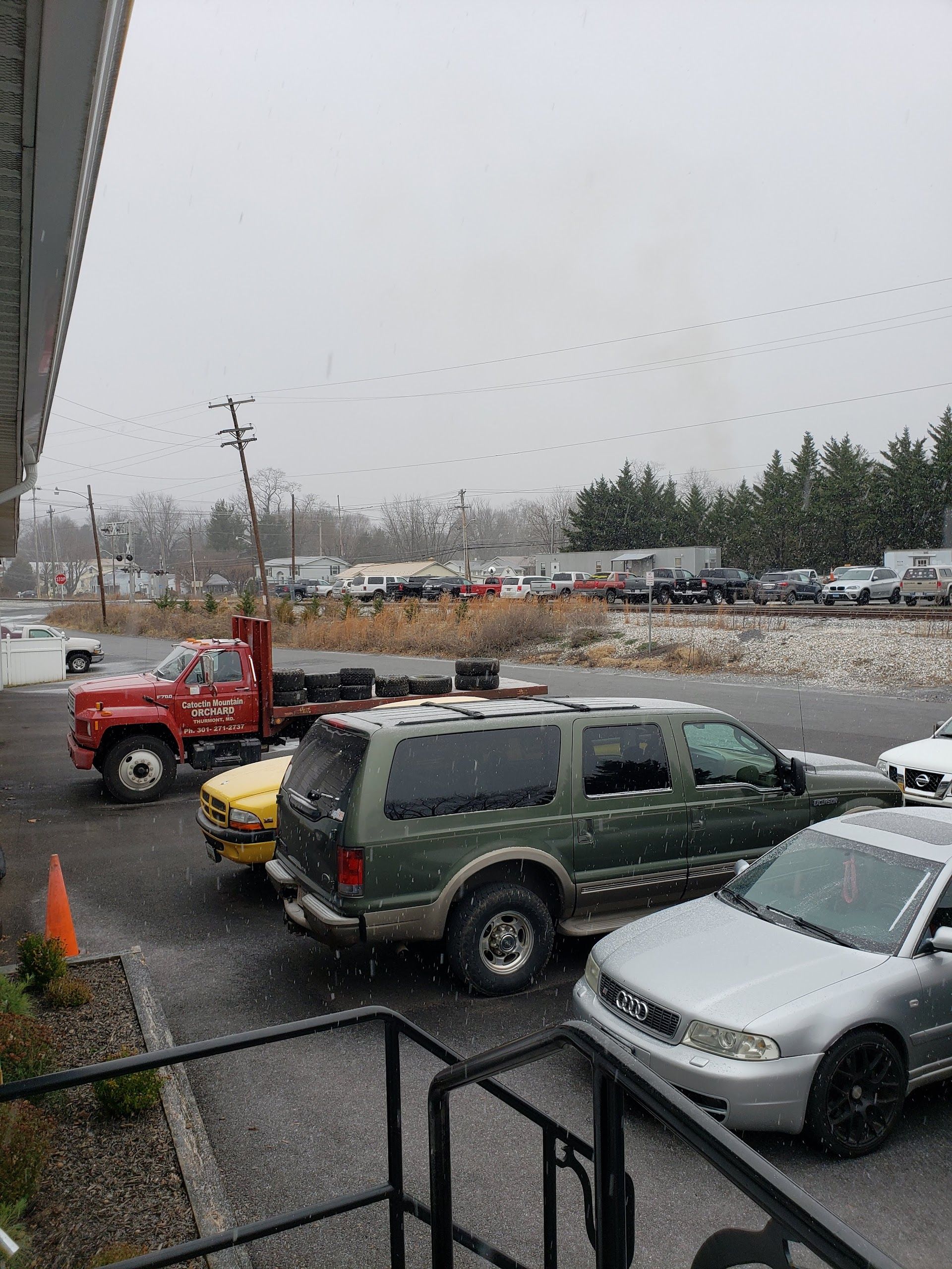 Snowy scene with cars parked outside a building, including a red truck, green SUV, and silver sedan | Gateway Automotive Inc.
