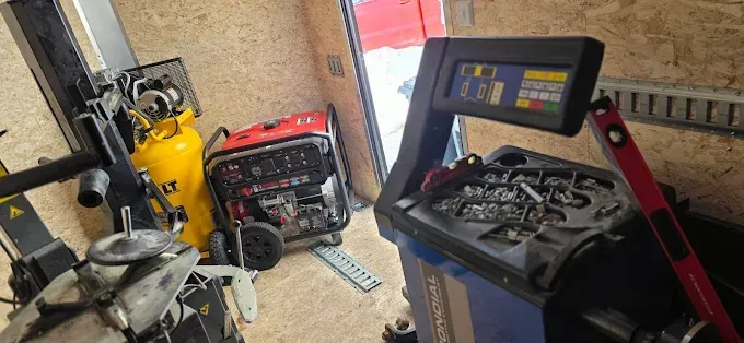 Scène d'atelier avec un compresseur d'air jaune, un générateur rouge et un chariot à outils bleu contenant des pièces et un moniteur.