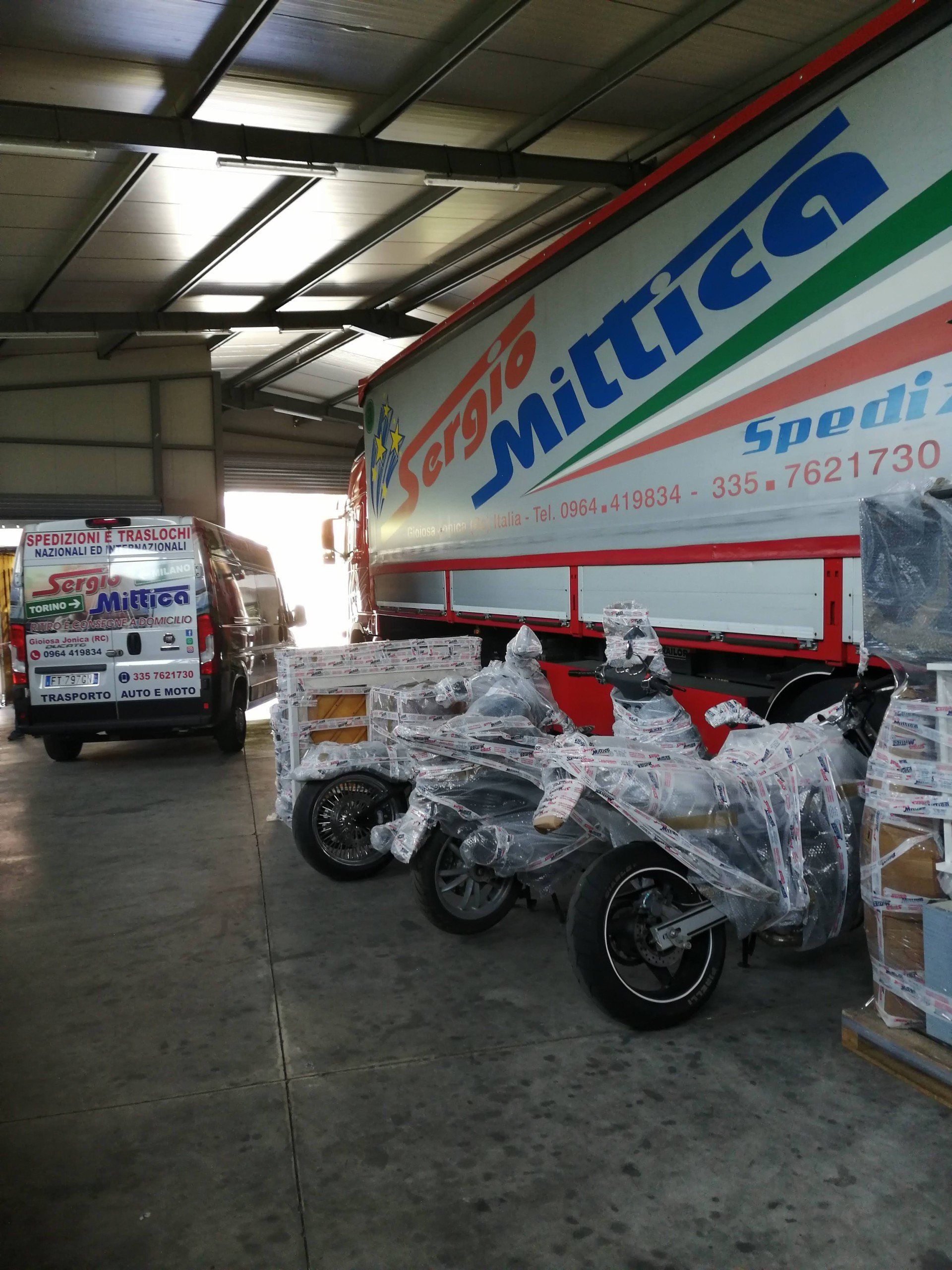 Camion Sergio rosso parcheggiato nell'area di carico di un magazzino, vista frontale con rimorchio bianco e cabina rossa.