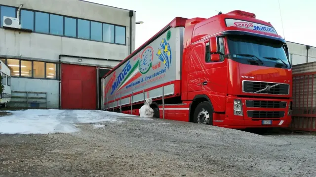 Camion delle consegne rosso parcheggiato accanto a un edificio industriale con una porta rossa e terreno innevato.
