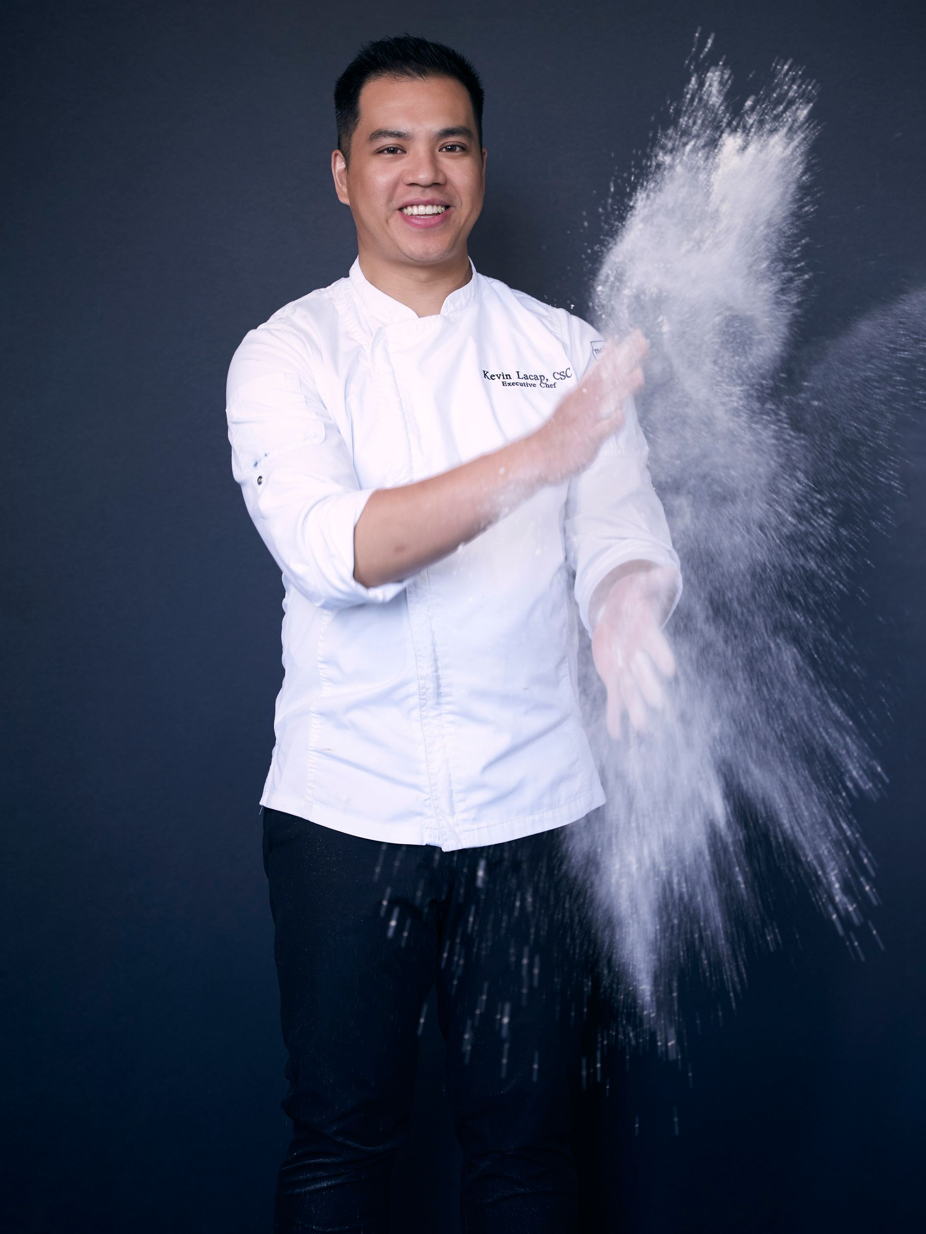 Chef serving food at a buffet table with stacks of white plates, in a well-lit modern setting.