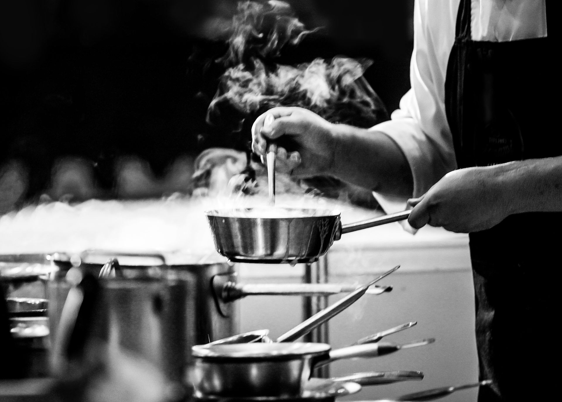 Chef cooking, stirring a pot over a stove with steam rising, in a commercial kitchen.