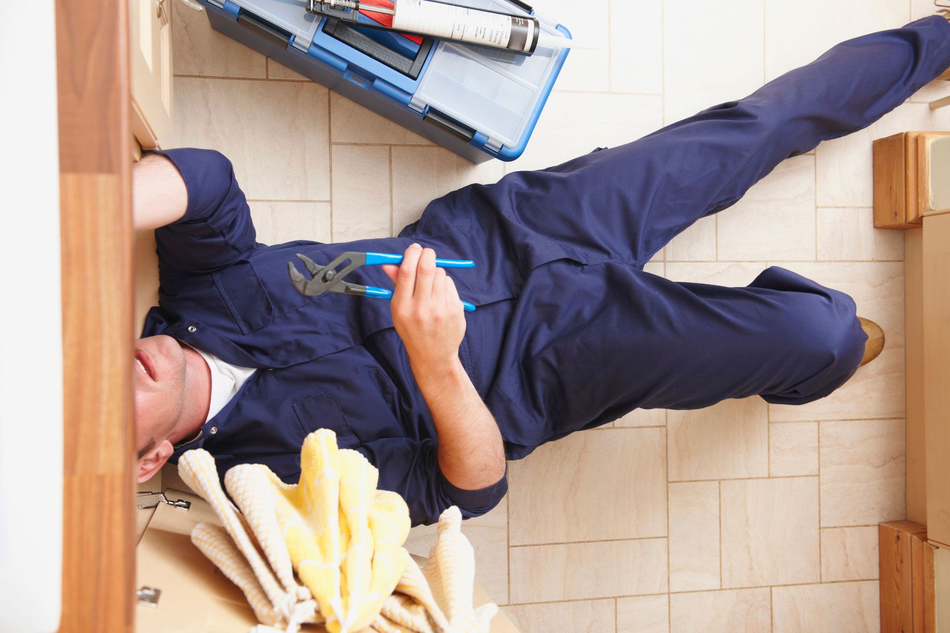 A plumber checking for leaks under a sink as part of a plumbing maintenance service. A plumber checking for leaks under a sink as part of a plumbing maintenance service.