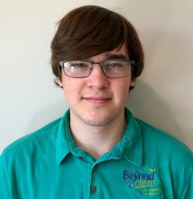 A young man wearing glasses and a green shirt that says beyond clean