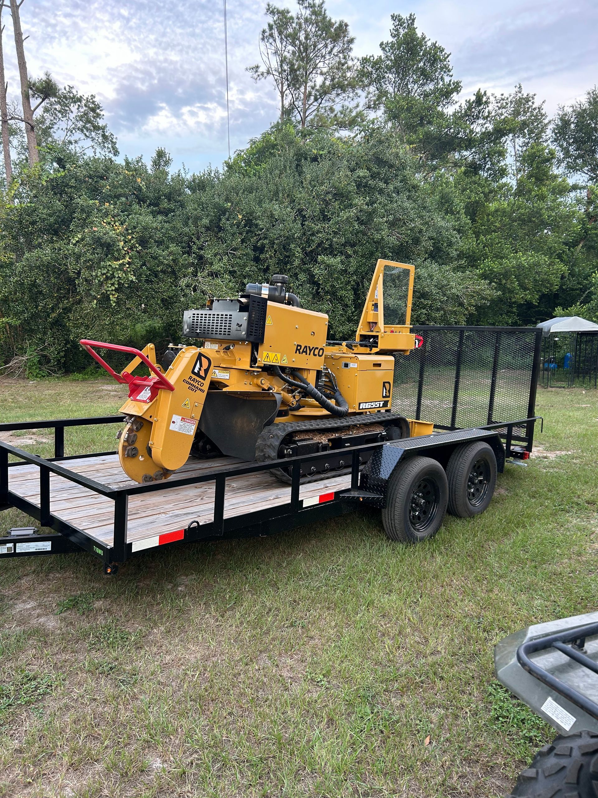 Yellow industrial machine on a black trailer in a grassy yard, with trees in the background.