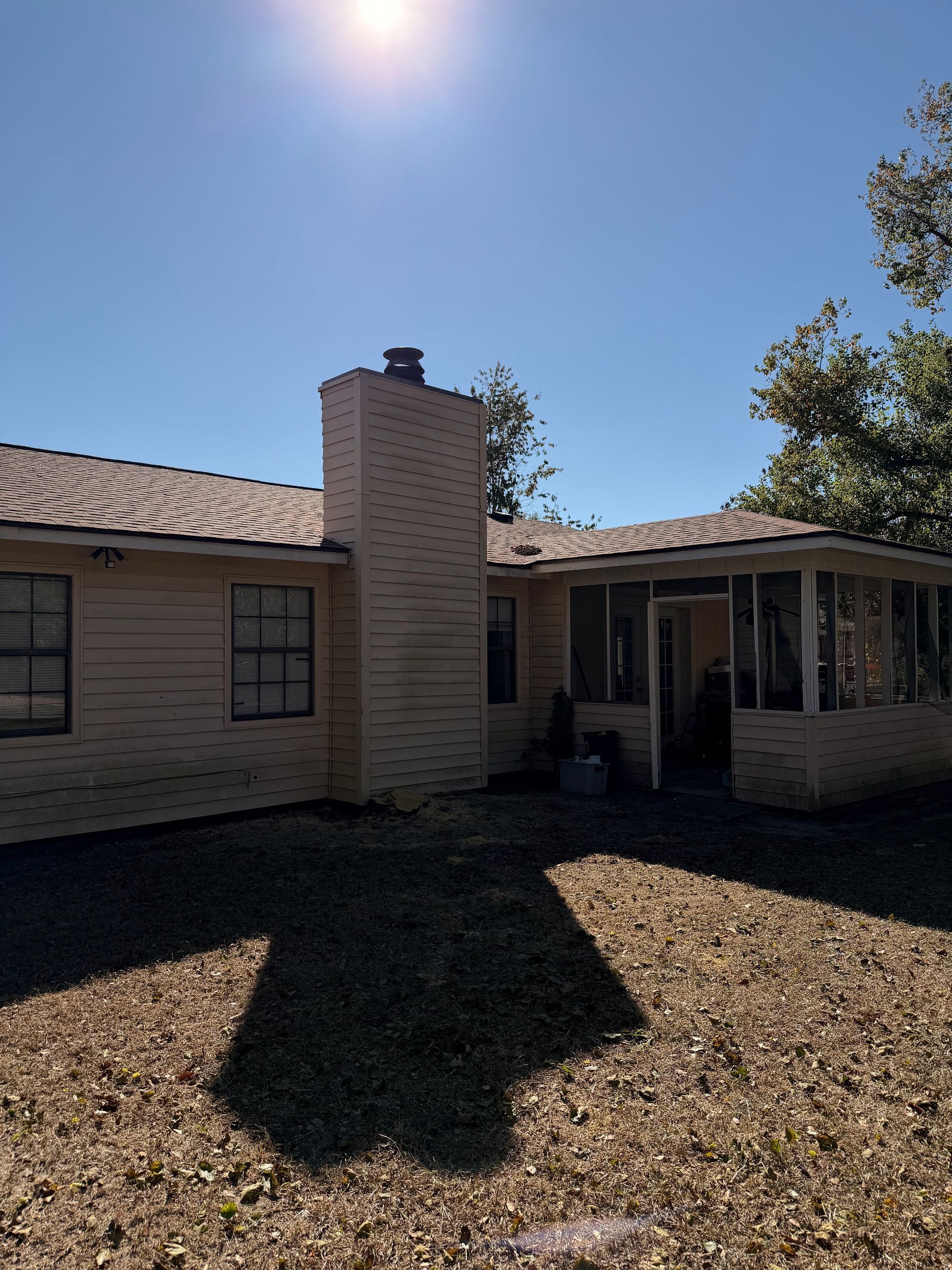 Single-story beige house with tiled roof, chimney, and shaded front yard under bright sun.