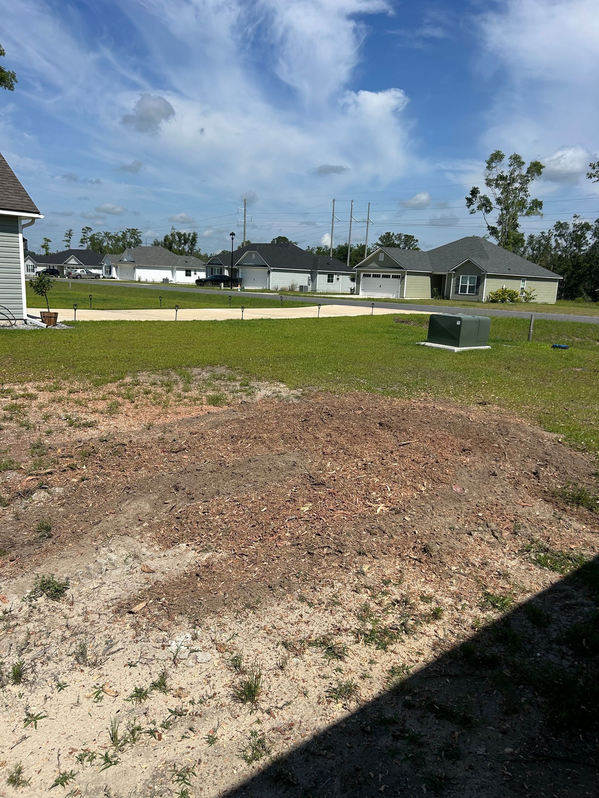 Empty grassy yard beside a suburban street under a partly cloudy blue sky