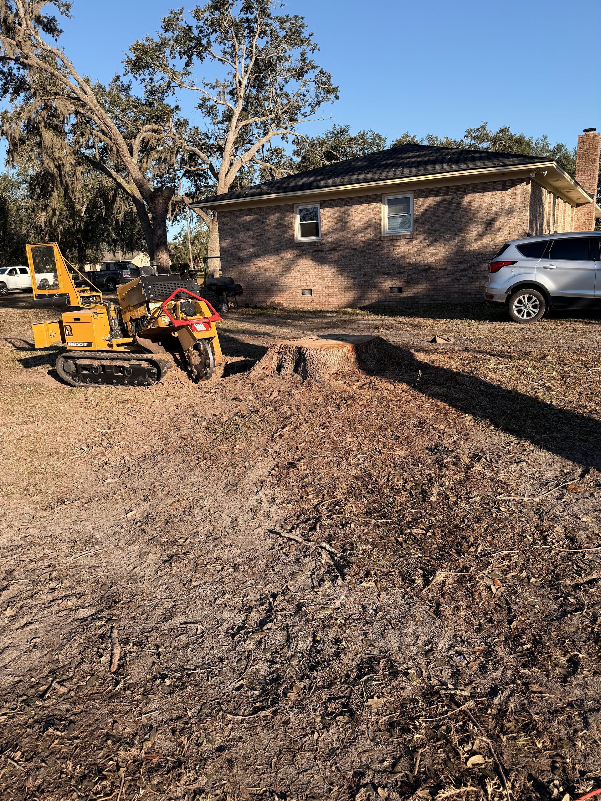 Yellow trencher with worker digging in a leaf-covered yard beside a brick house and parked SUV.