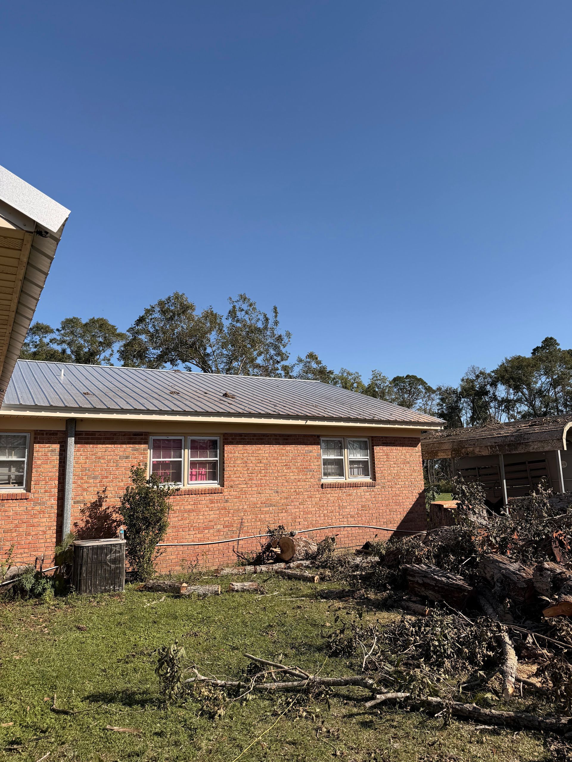 Brick house with a corrugated roof and a yard with bushes under a clear blue sky